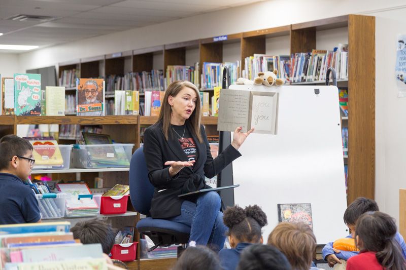 Dr. Gist reading to a group of elementary students in a school library.