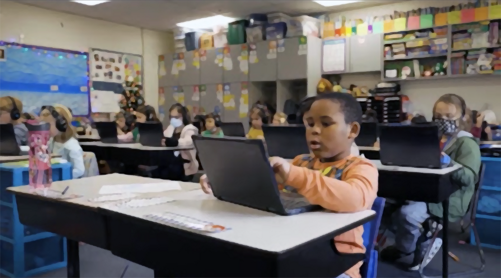 Students sitting at desks in clasrooms with laptops open in front of them.