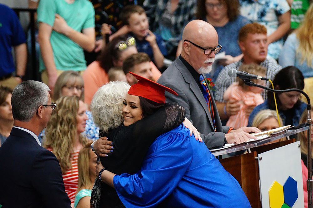 A graduate in a blue gown hugs a faculty member on stage at graduation ceremony 