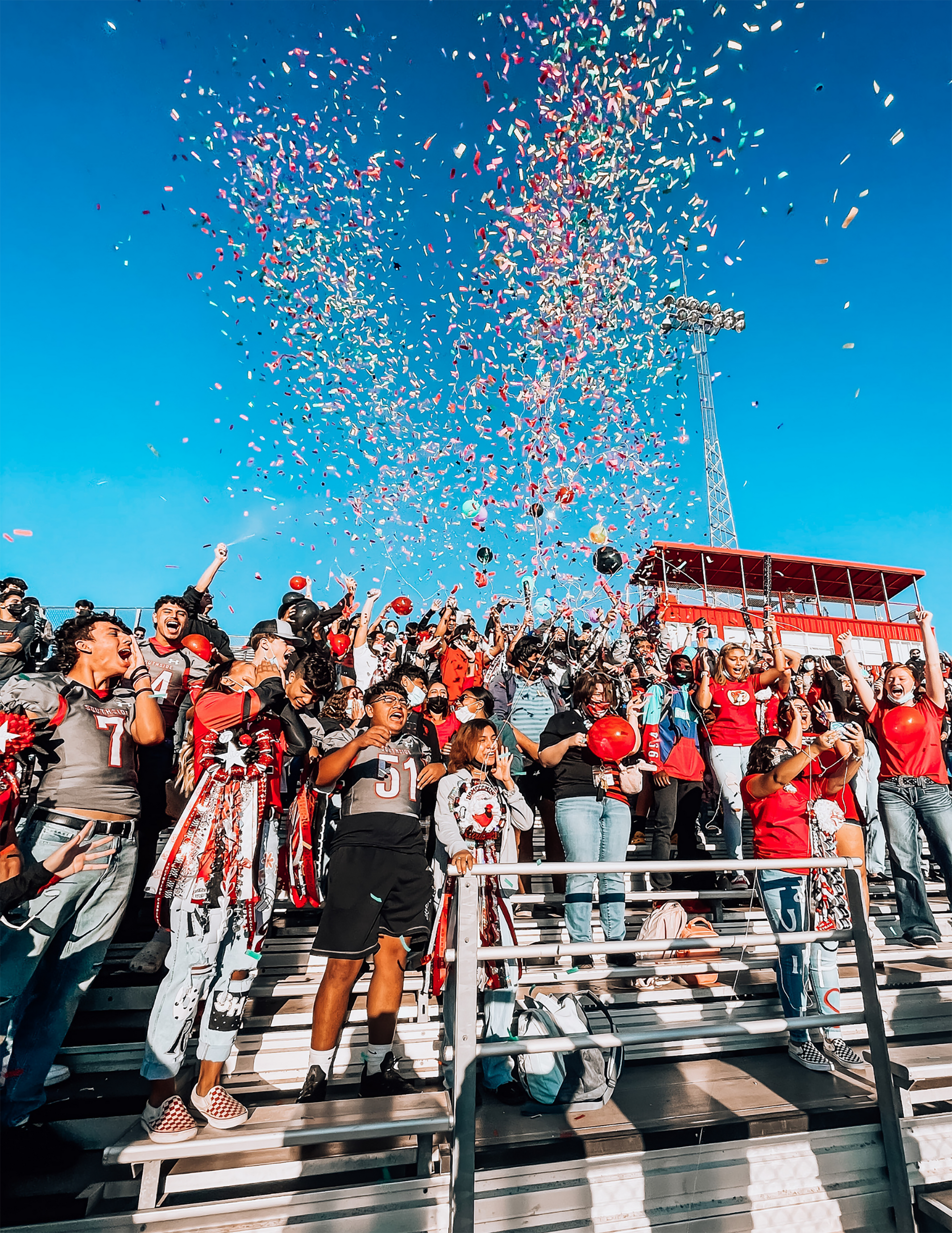 Crowd in the stands of a football stadium cheers with confetti in the air above them.