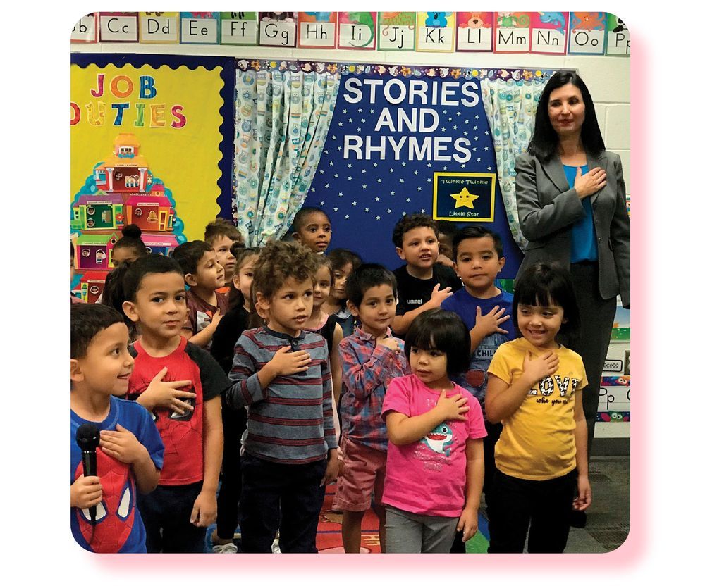 Dr. Hightower stands among a classroom of young students, all with hands on their hearts for a pledge. 