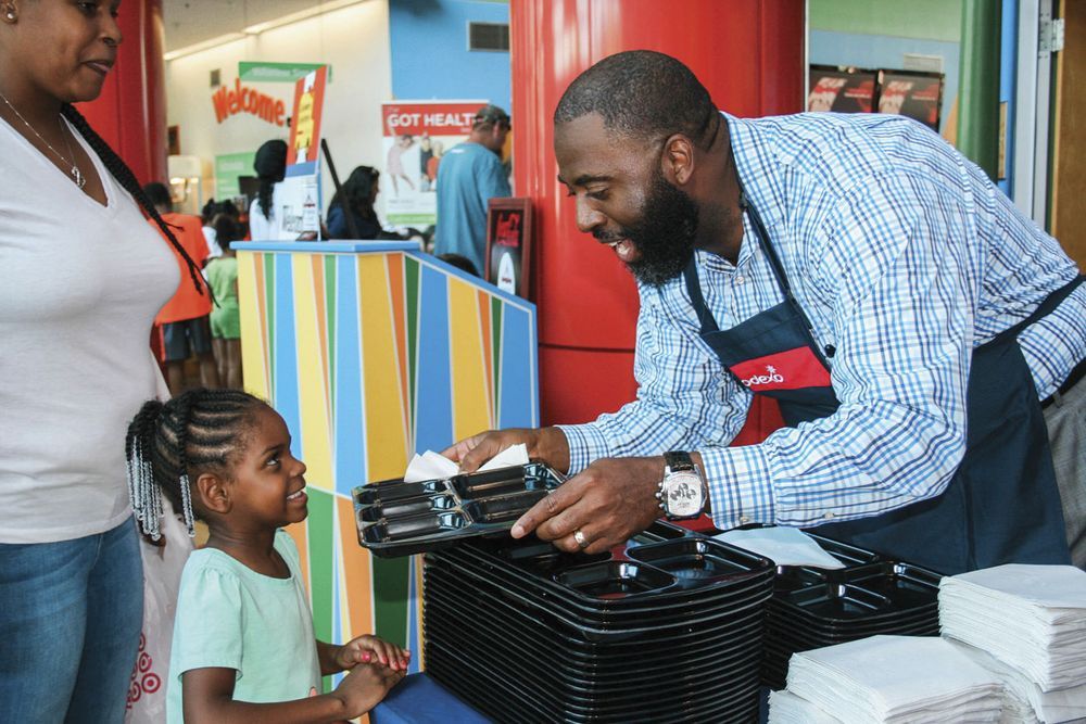 Photograph of Dr. Barron Davis handing a lunch tray to a smiling young student.