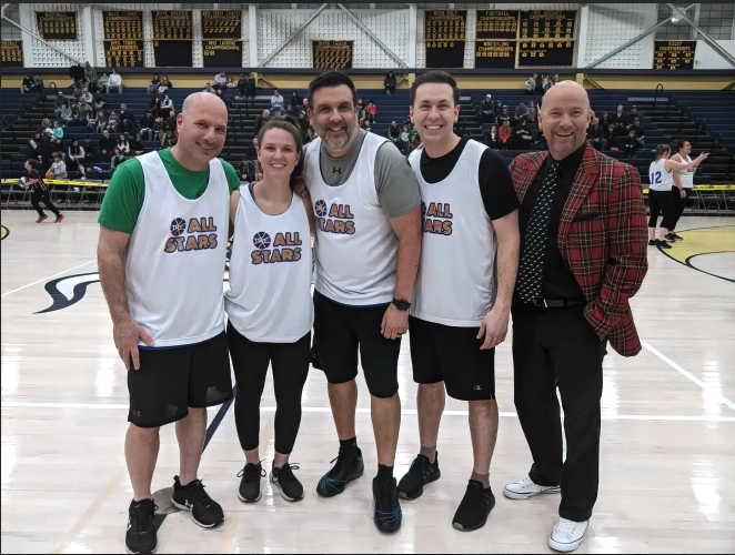 Photograph of Superintendent Dr. John Sanville standing with staff at a basketball game