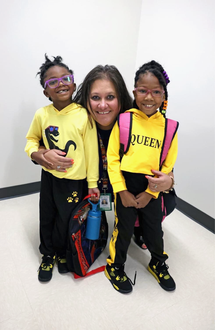 Photograph of Dr. Birhanzel kneeling down and smiling between two young students