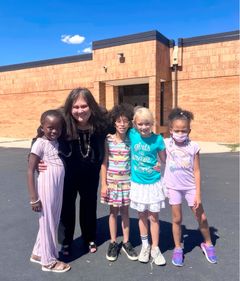 Photograph of Dr. Birhanzel posing with four students outside of a school building