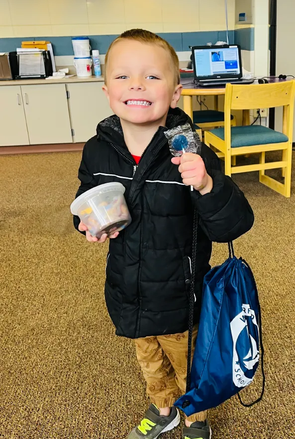 Photograph of a smiling elementary school student with lollipop and backpack